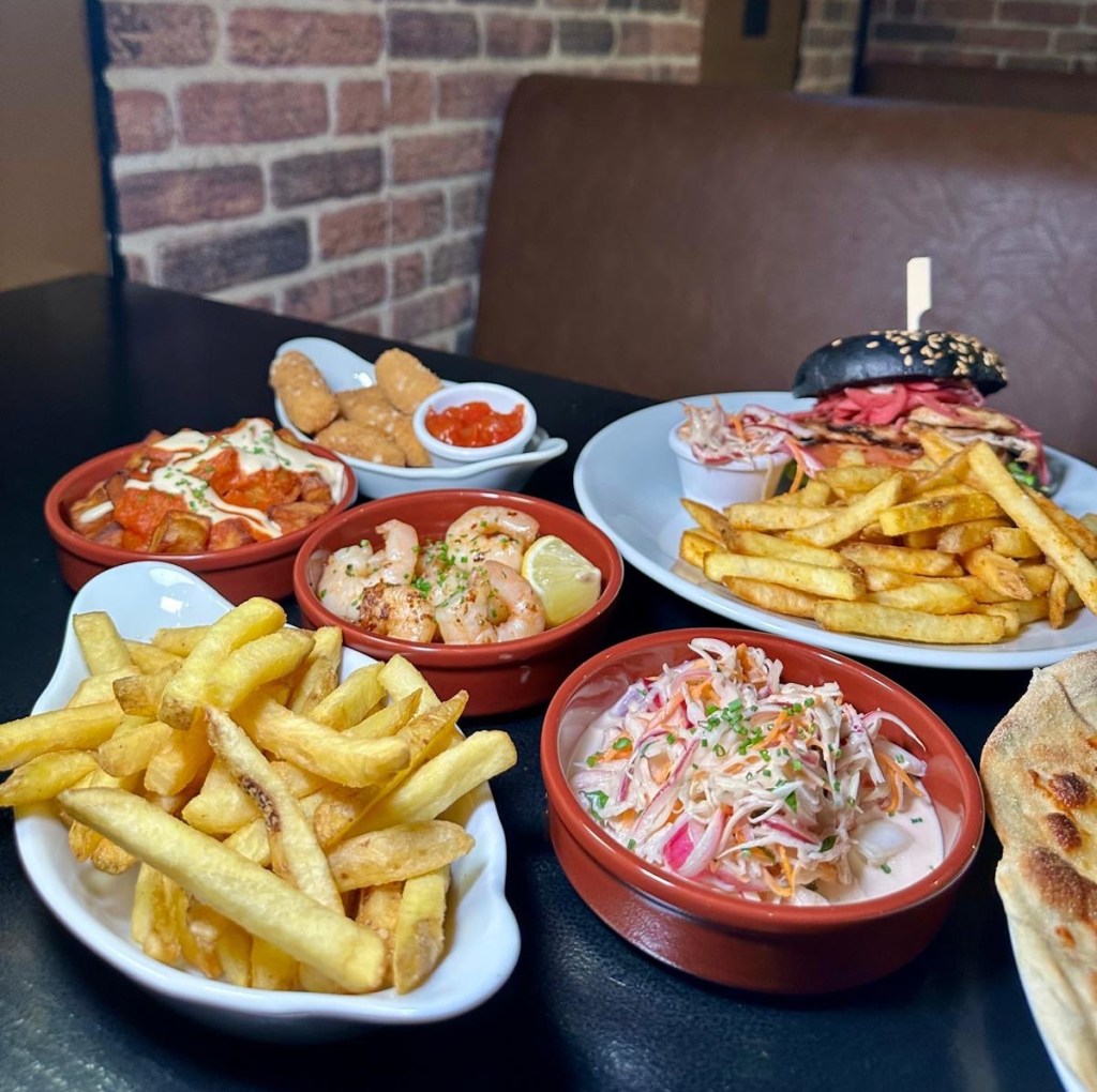 A variety of food at Abajo sports bar, including a Blackened Cajun Burger, Gambas Pil Pil, Patatas Bravas, Mac & Cheese Bites, and garlic bread.