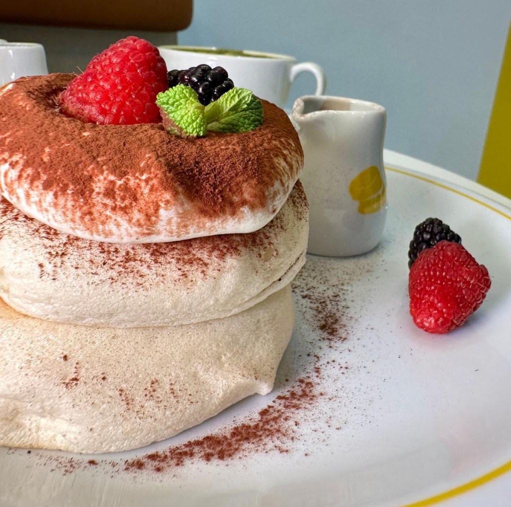 Tiramisu-flavored soufflé pancakes with creamy topping and cocoa powder dusting, served on a dessert plate.