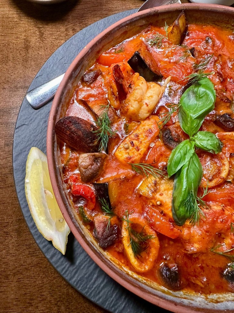 A steaming seafood casserole with prawns, mussels, squid, and salmon, baked in a creamy tomato-garlic sauce, served in a rustic clay pot