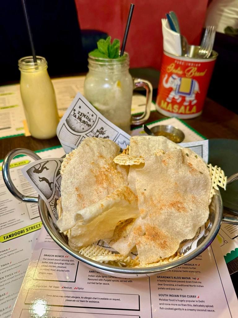 A basket of golden, crispy popadoms served with vibrant chutneys and dips in small bowls