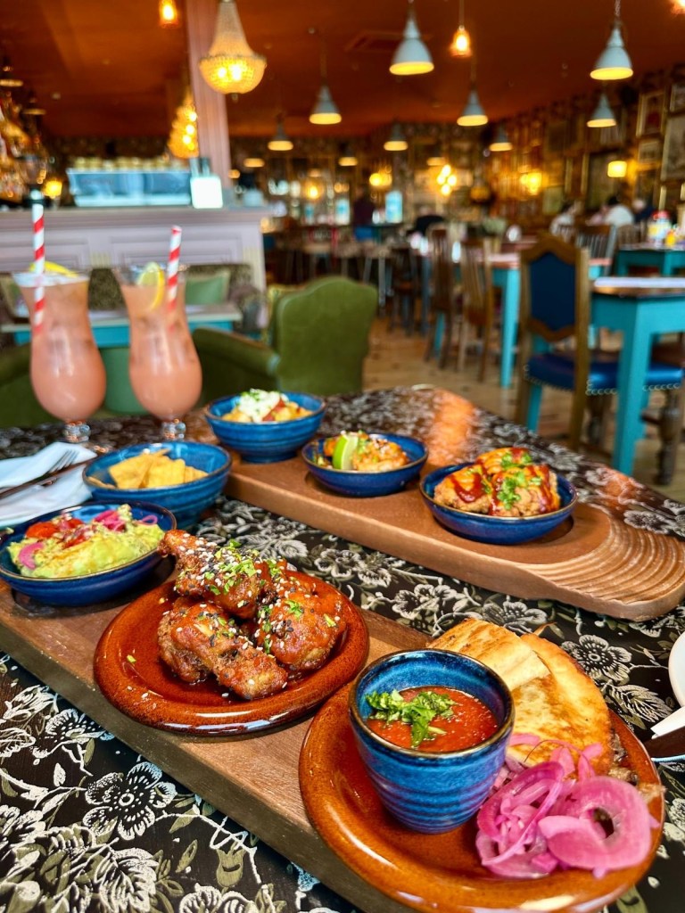 A tapas spread featuring patatas bravas, Korean king prawns, fried cauliflower, quesadillas, chicken wings, and guacamole with tortilla chips.