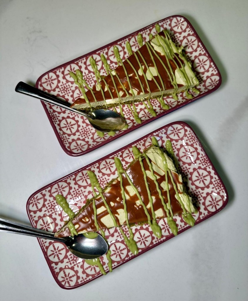 A slice of luxurious Dubai Cheesecake with a rich, creamy filling, topped with crushed pistachios and a drizzle of syrup, all resting on a baklava-inspired base.