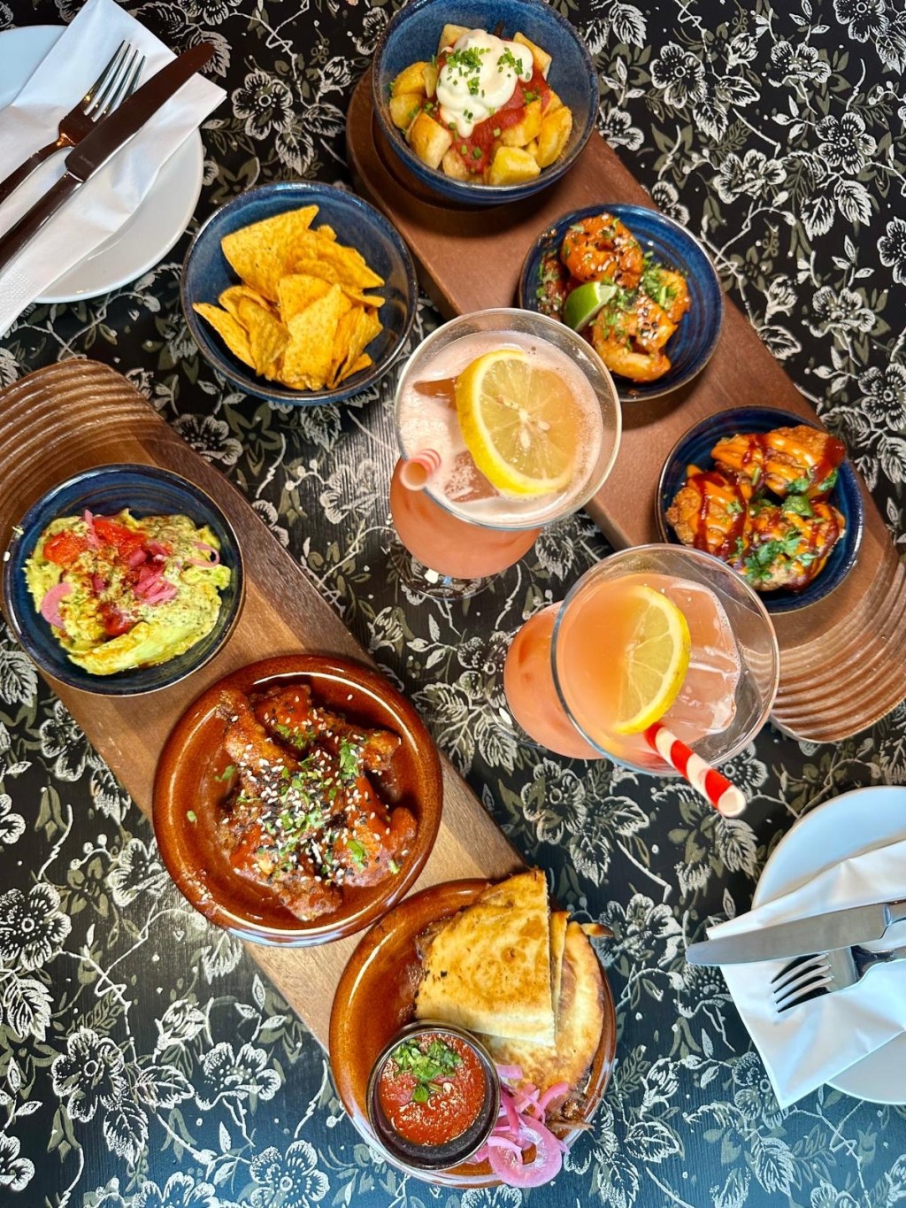 A tapas spread featuring patatas bravas, Korean king prawns, fried cauliflower, quesadillas, chicken wings, and guacamole with tortilla chips.
