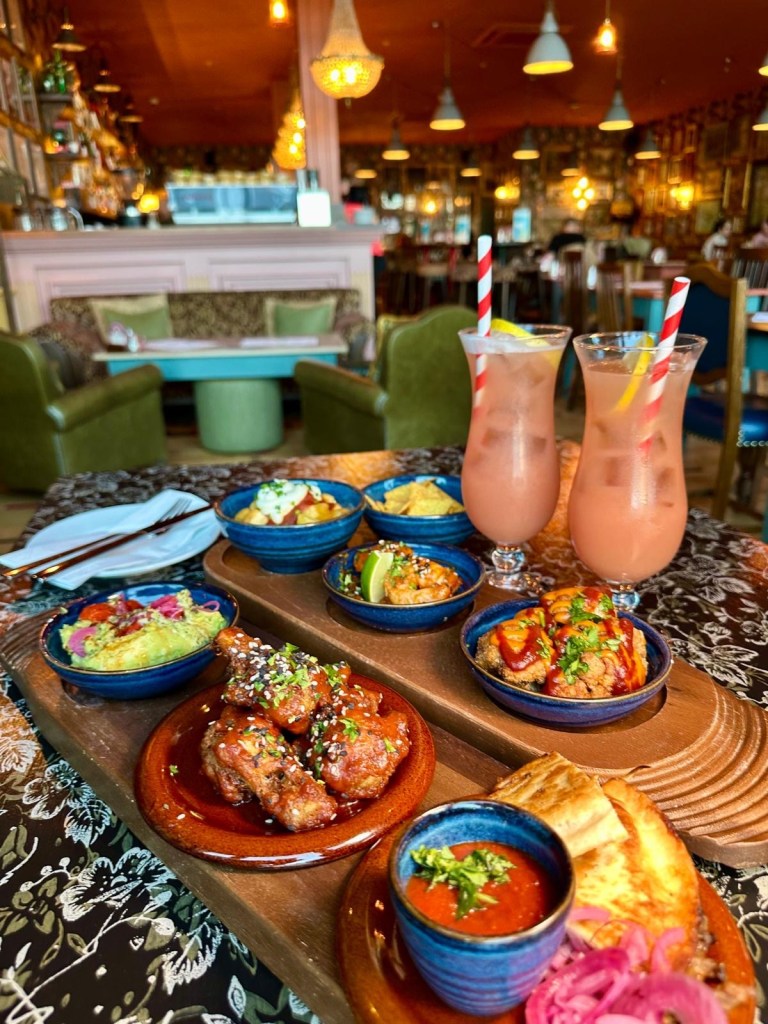 A tapas spread featuring patatas bravas, Korean king prawns, fried cauliflower, quesadillas, chicken wings, and guacamole with tortilla chips.