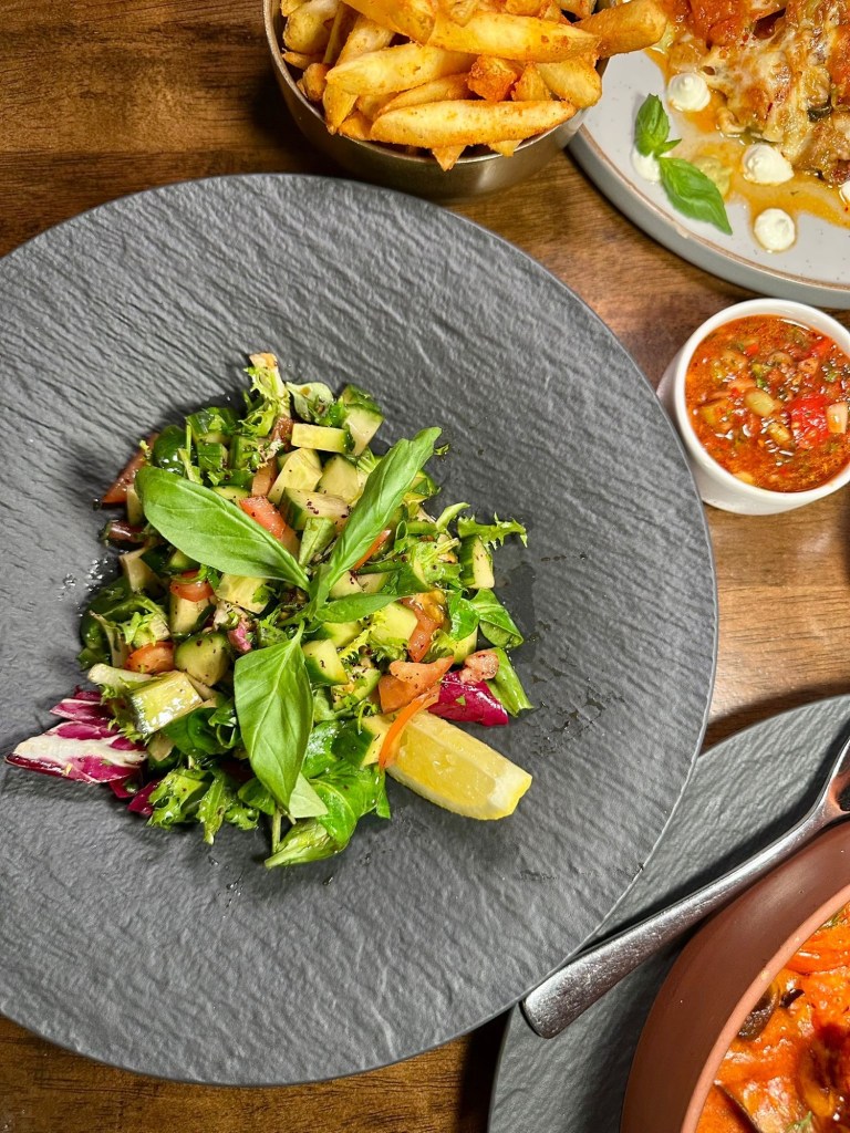 A vibrant Mediterranean salad featuring fresh greens, juicy tomatoes, crisp cucumbers, and red onions, drizzled with a sweet and tangy pomegranate molasses dressing, topped with a lemon wedge for an extra zesty kick