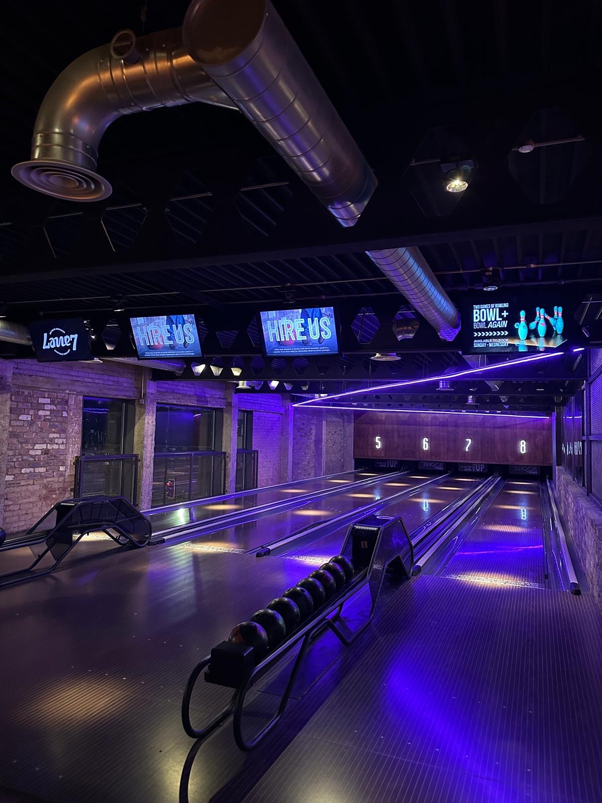 A stylish bowling alley with neon lights illuminating the lanes and a buzzing crowd enjoying a game.
