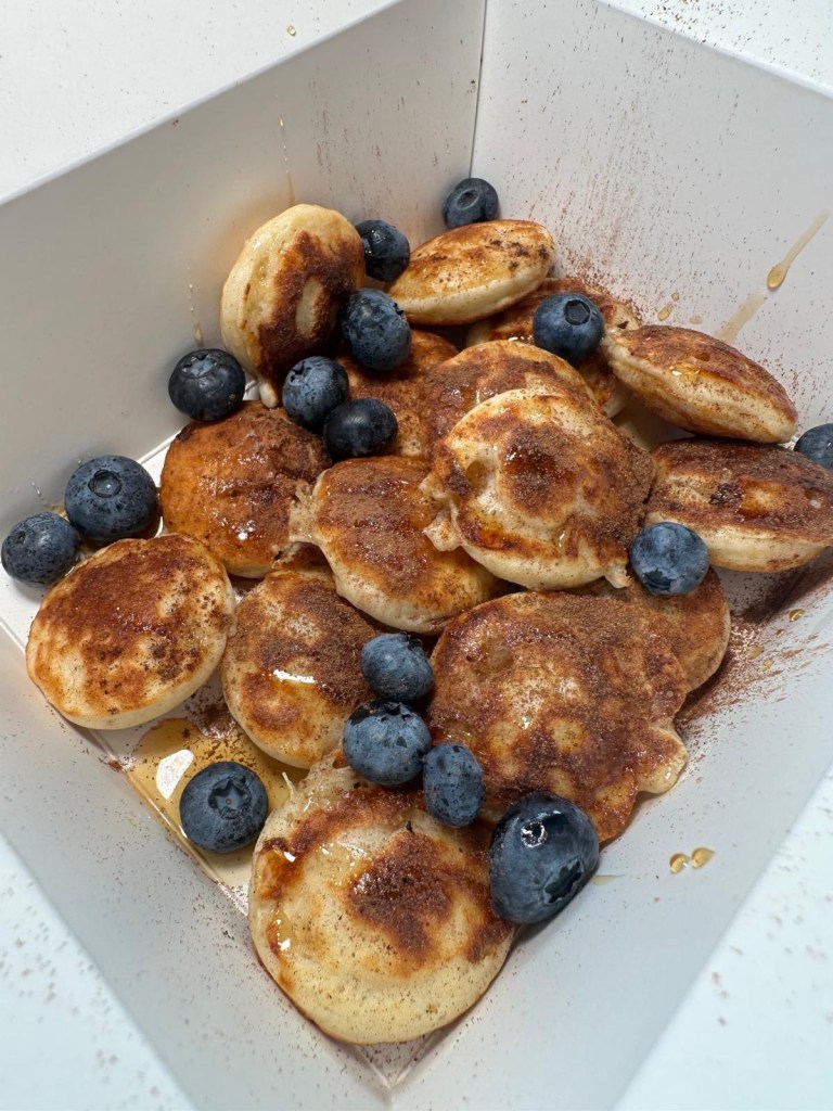 A box of golden protein pancake balls, drizzled with syrup and topped with fresh blueberries, served at Eat Clean in Whitley Bay.