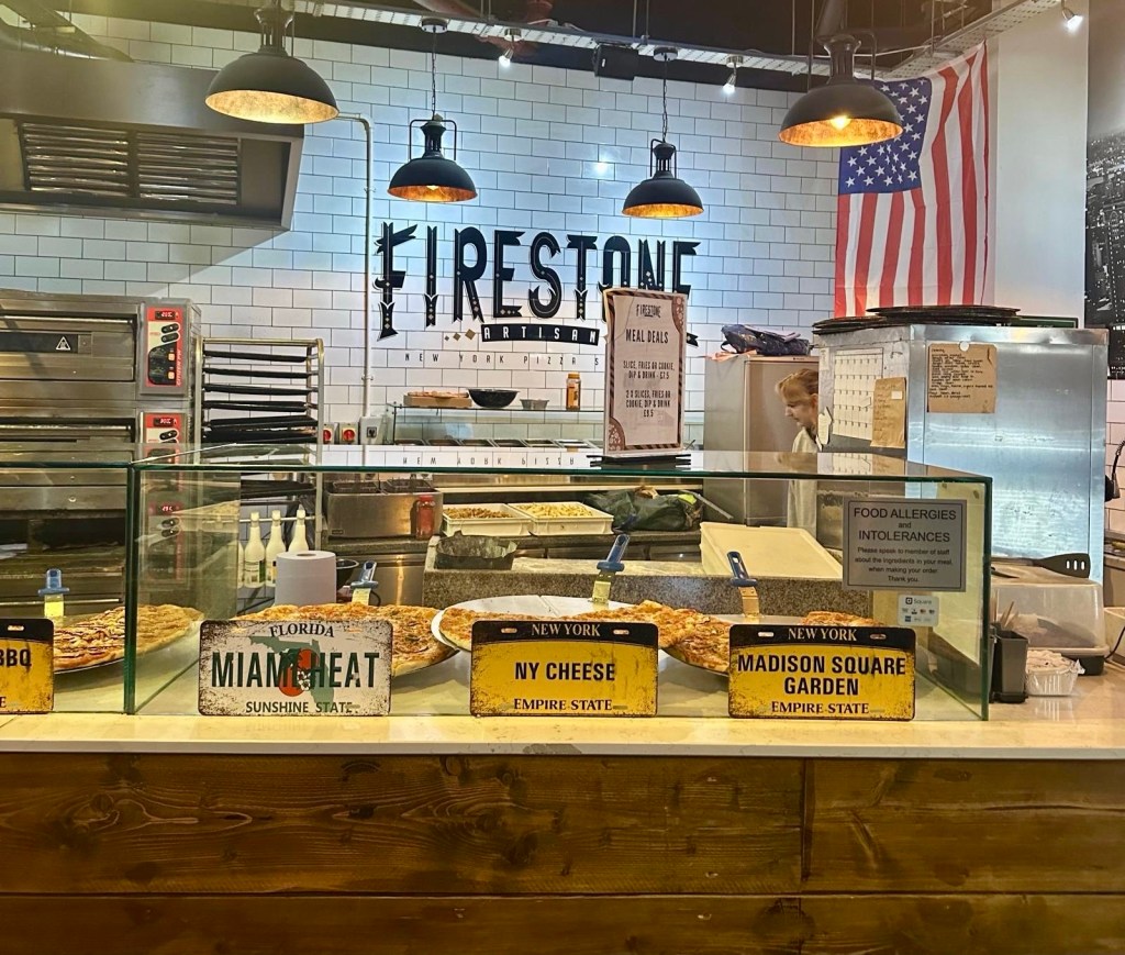 The interior of Firestone Artisan Pizza featuring NYC-inspired decor, industrial-style lighting, and New York street signs.