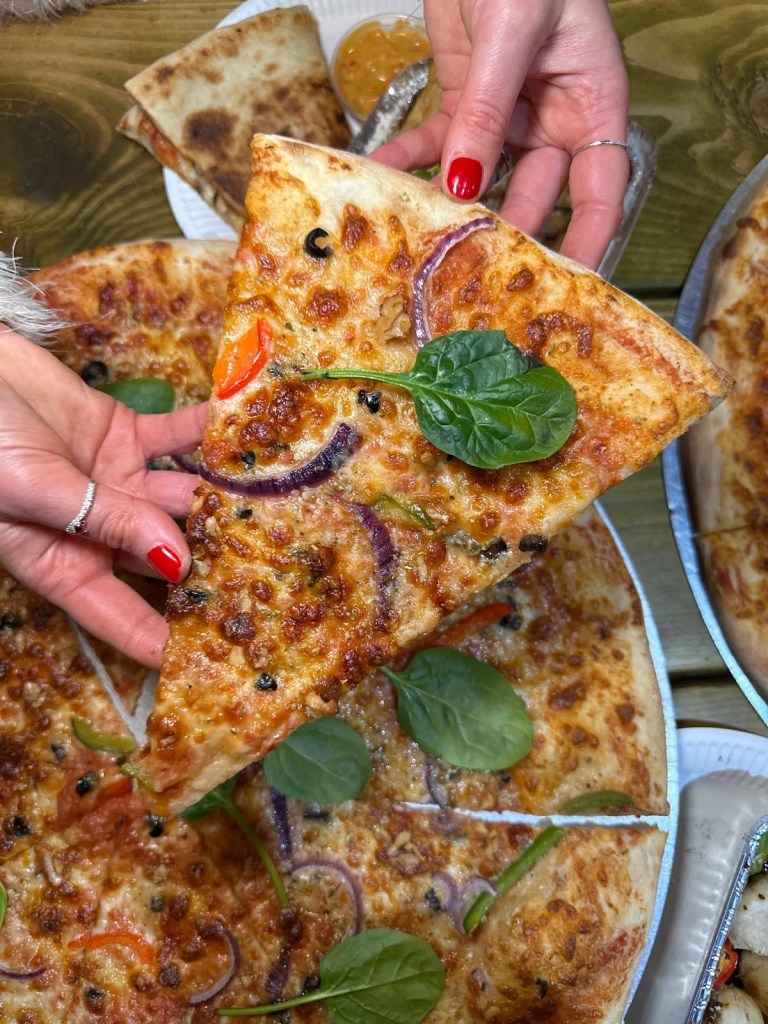 A gourmet truffle-infused New York-style pizza topped with mozzarella, red onion, walnuts, and spinach on a tomato base.