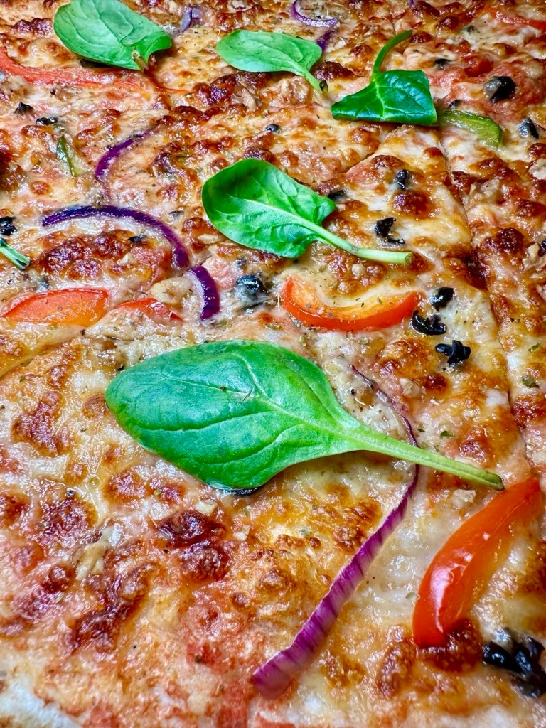 A gourmet truffle-infused New York-style pizza topped with mozzarella, red onion, walnuts, and spinach on a tomato base.