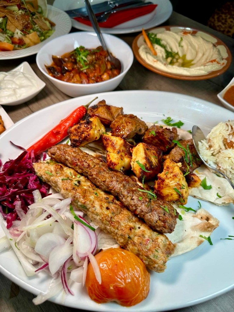 Beyruty Mixed Grill featuring charcoal-grilled kafta lamb, lamb shish, chicken cubes, and koftah, served sizzling hot.