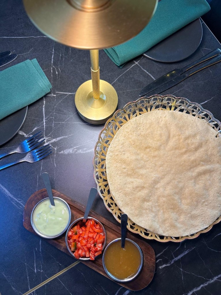 A vibrant pickle tray featuring crispy poppadoms, a selection of chutneys, and a unique onion salad coated in a sweet masala-based sauce. A perfect mix of traditional and modern flavors.