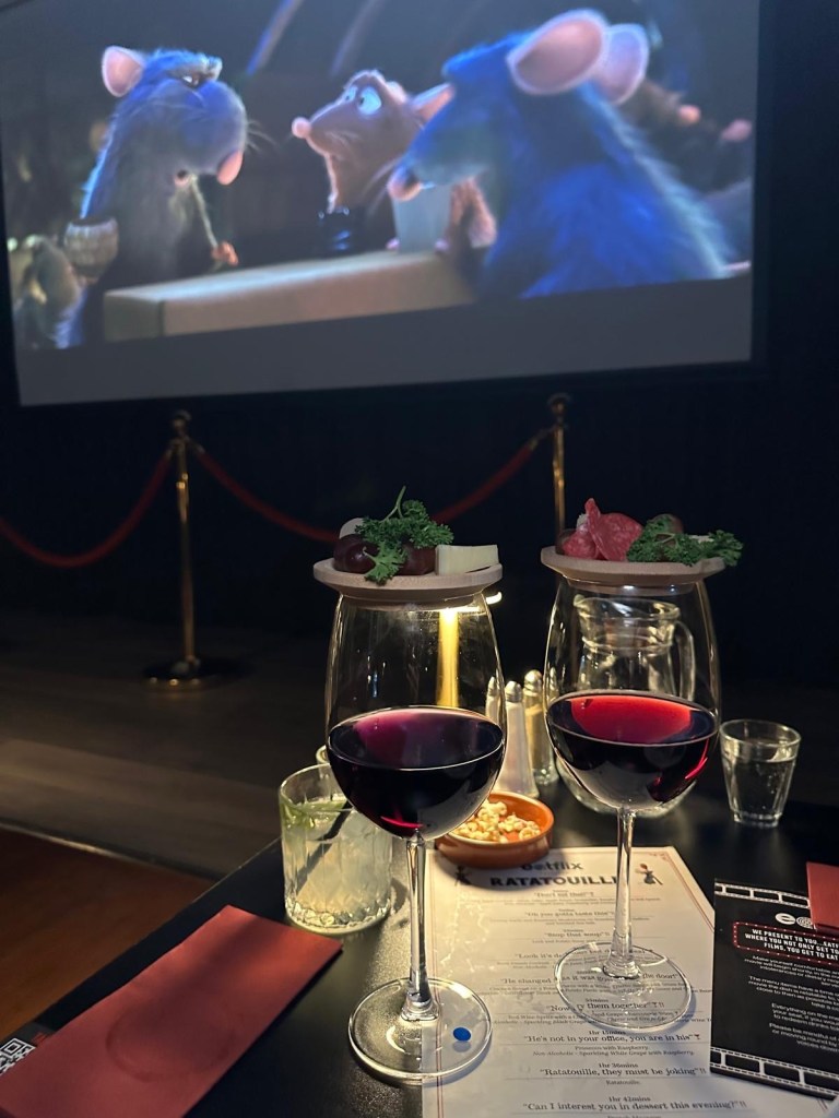 A glass of red wine spritz with a mini cheese and grape charcuterie skewer balanced on top.