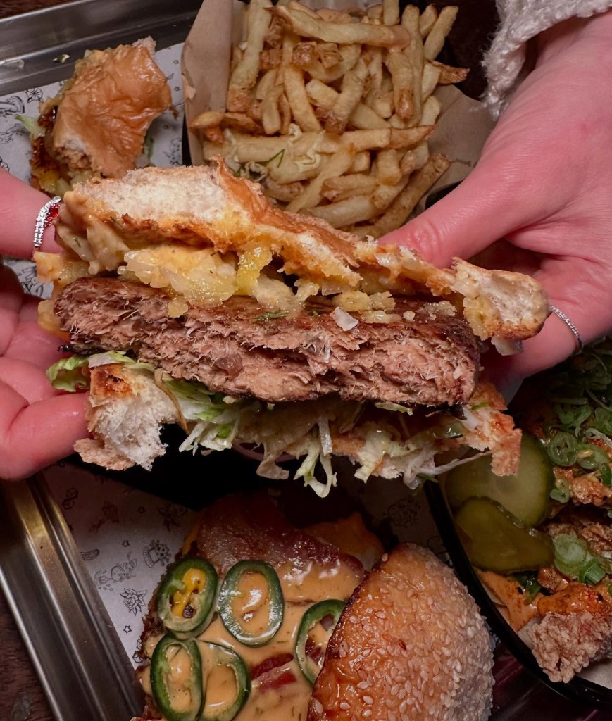 A plant-based Moving Mountains burger with smoked cheddar, shredded lettuce, diced onions, and house sauce in a soft bun.