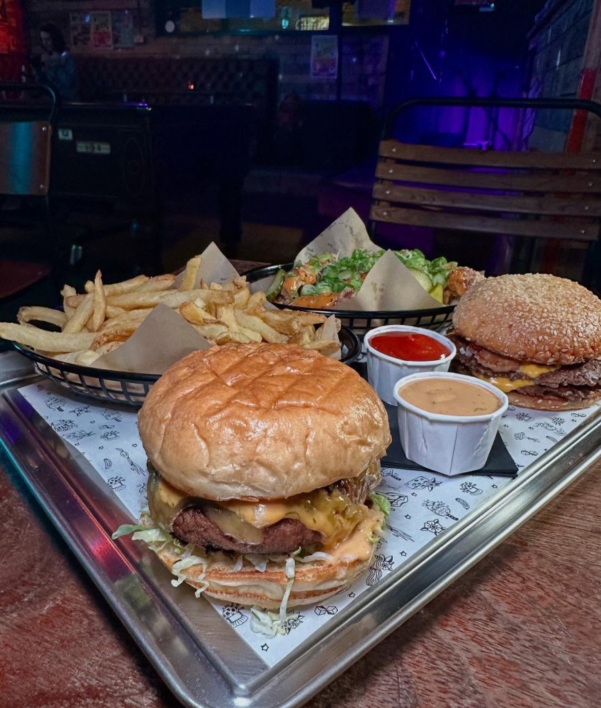 A spread of Pattymelts' top menu items, including stacked burgers, crispy fries, hot fried chicken, house sauce, and burnt Basque cheesecake.