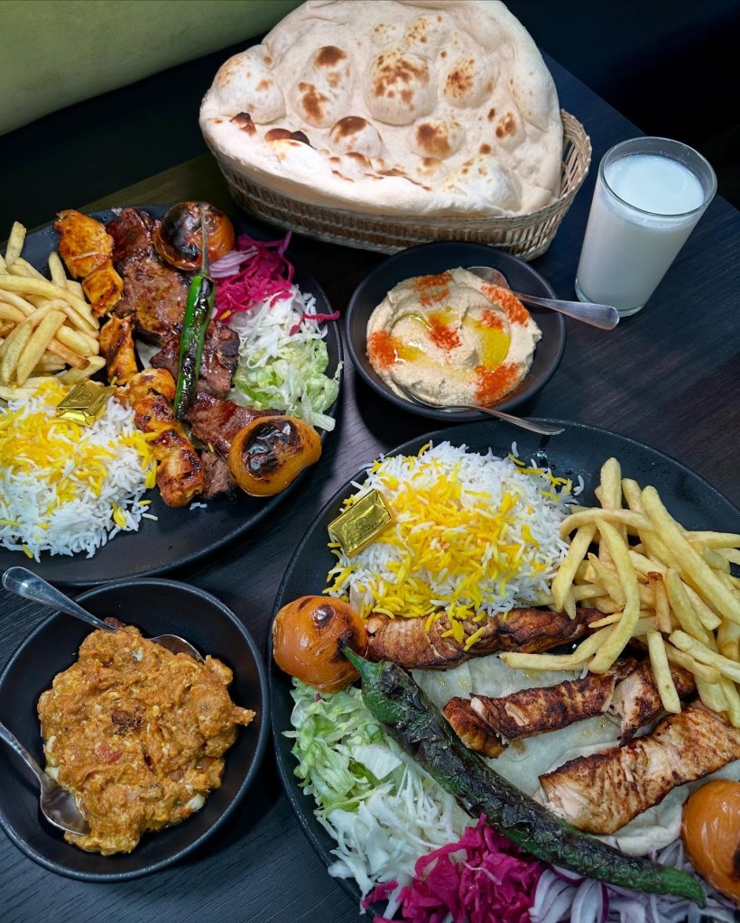 A spread of Persian dishes including chargrilled salmon, lamb chops, grilled aubergine, fresh salad, hummus, and baklava.