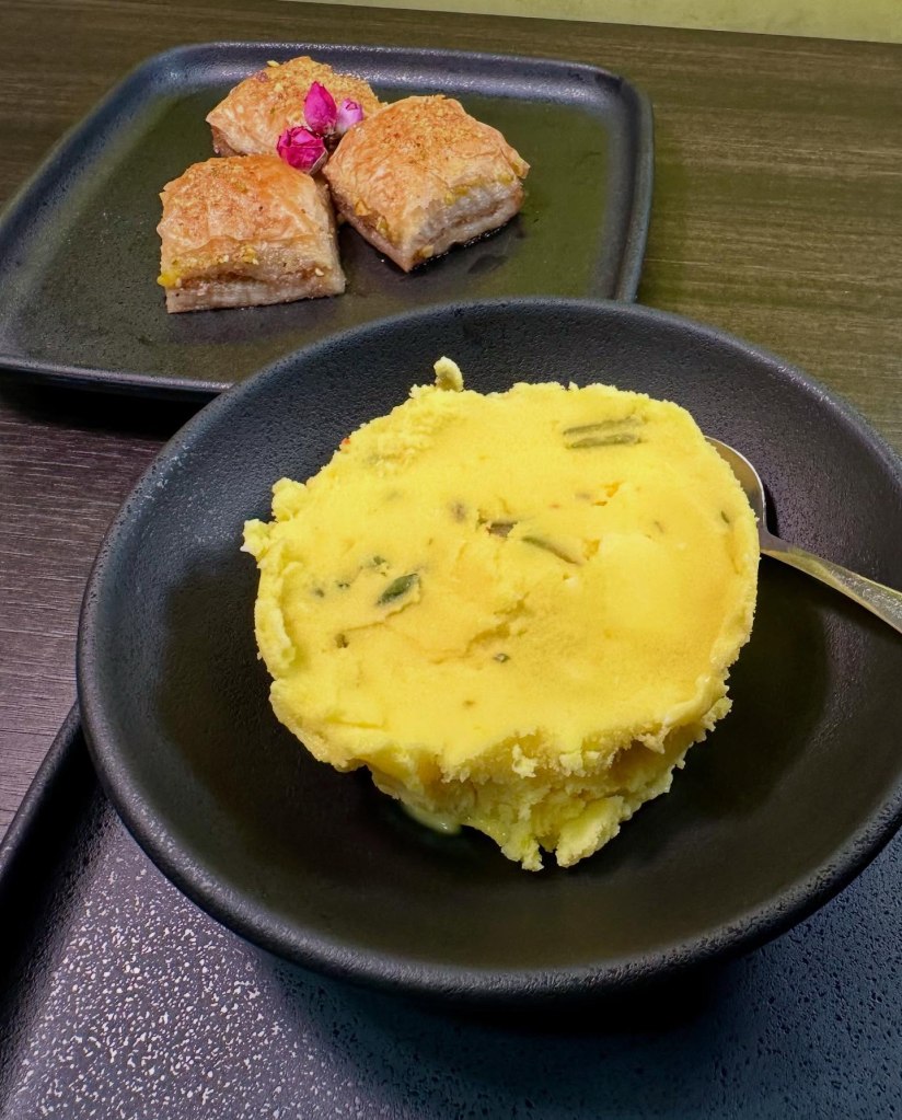 A scoop of Persian saffron ice cream with chopped pistachios, served in a small bowl.