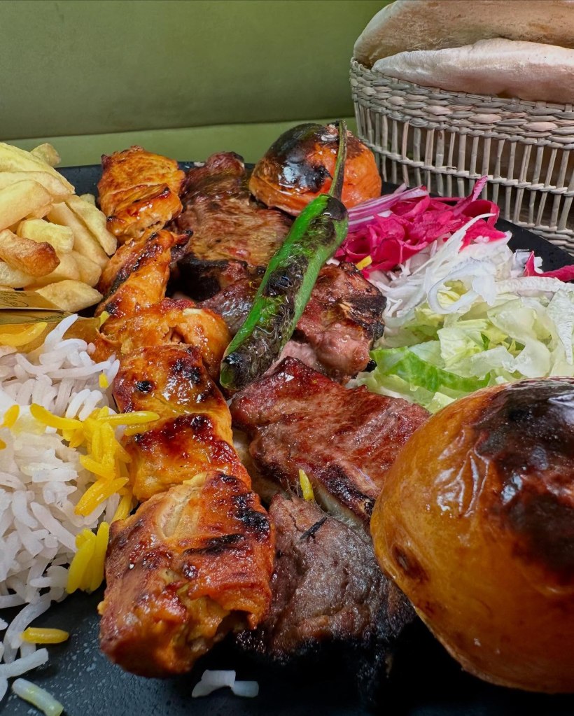 A plate of grilled lamb chops and chicken skewers, accompanied by charred vegetables and a fresh side salad
