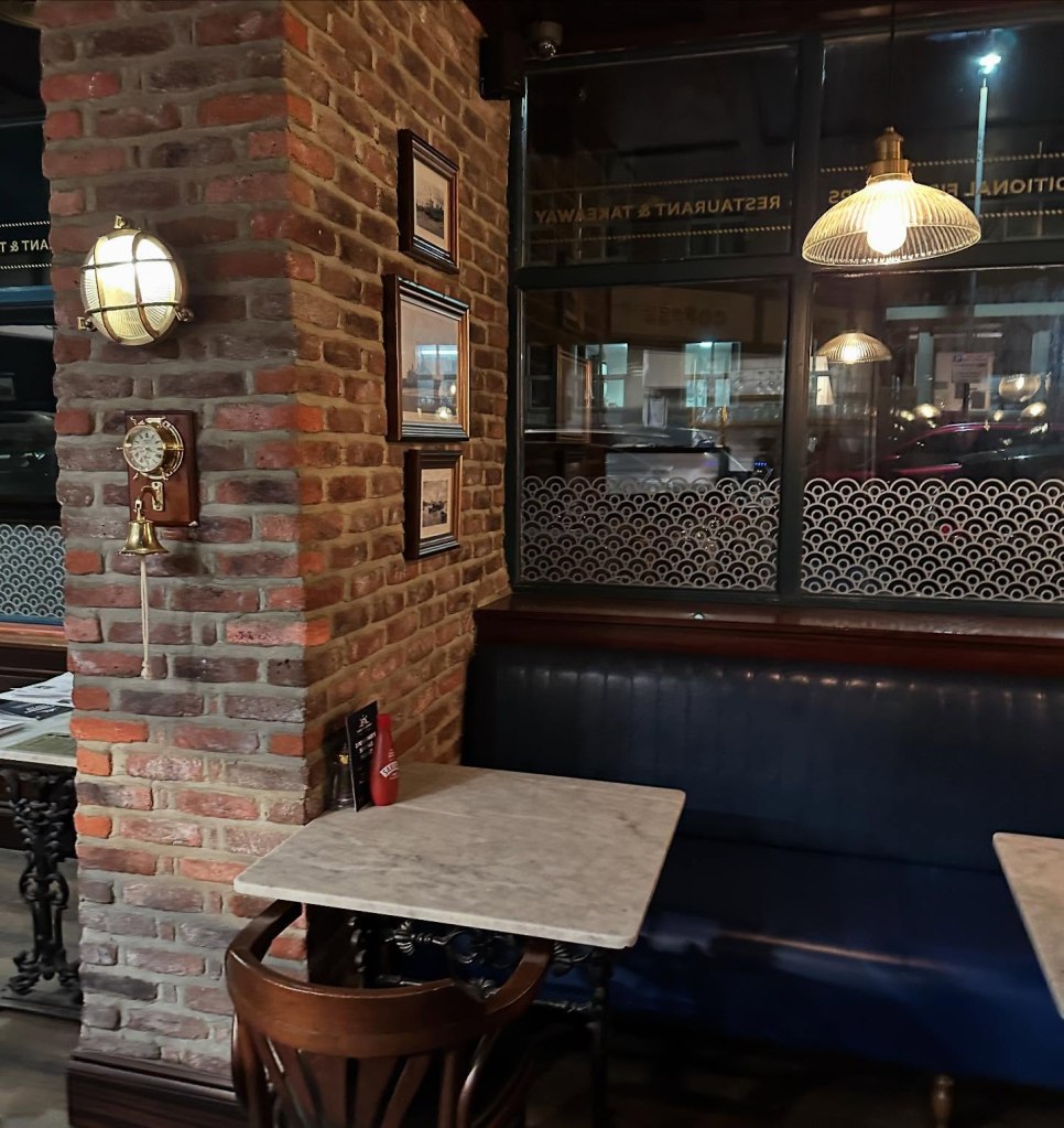 Cozy and welcoming interior of Fisherman’s Bay, featuring modern coastal decor, wooden tables, and large windows with a view of the seaside.