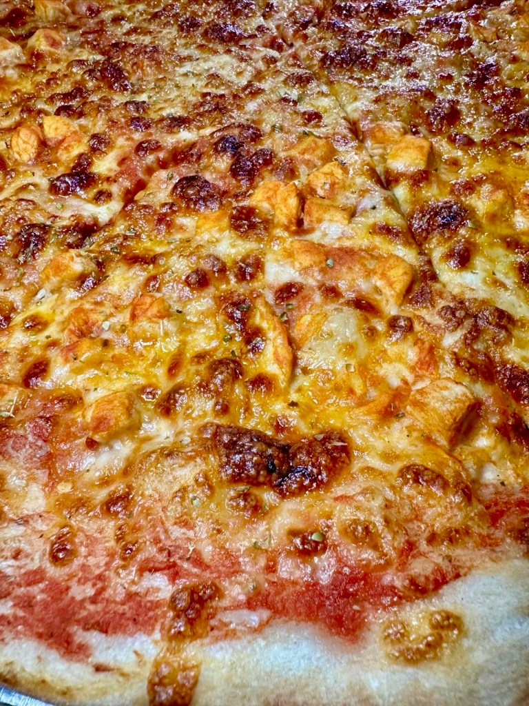 A slice of Buffalo chicken pizza topped with finely chopped buffalo-marinated chicken, melted mozzarella, and a classic tomato base.