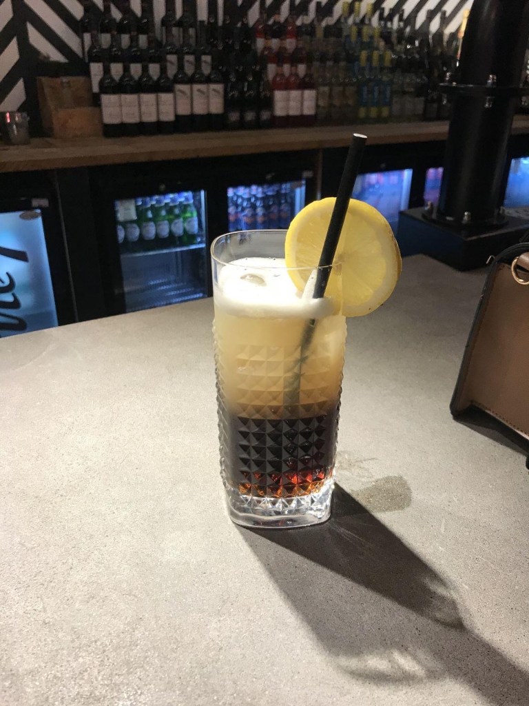 A mocktail in a highball glass with ice, garnished with a citrus slice and fresh mint.