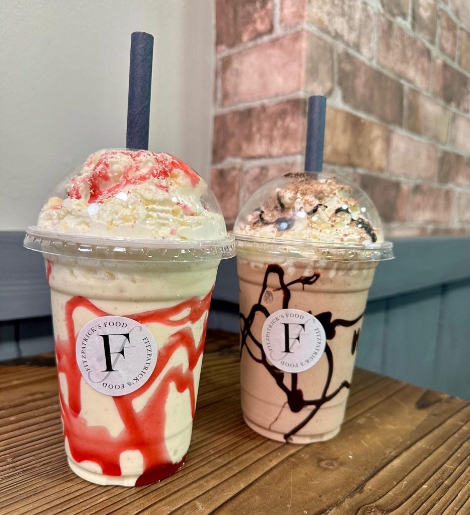 A creamy, thick milkshake served in a tall cup with whipped cream on top, available in a variety of flavors at Fitzpatrick’s Food.