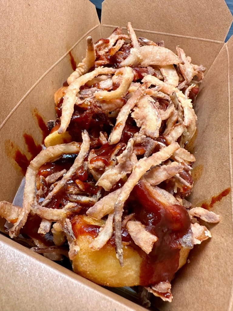 A generous portion of loaded fries topped with BBQ pulled pork and crispy onions, served in a takeaway tray.