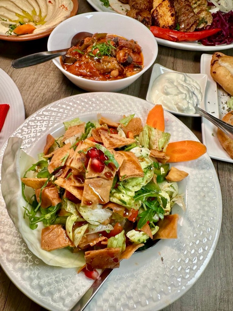 Fresh Beyruty Salad with crisp lettuce, tomato, cucumber, parsley, lemon dressing, and pomegranate