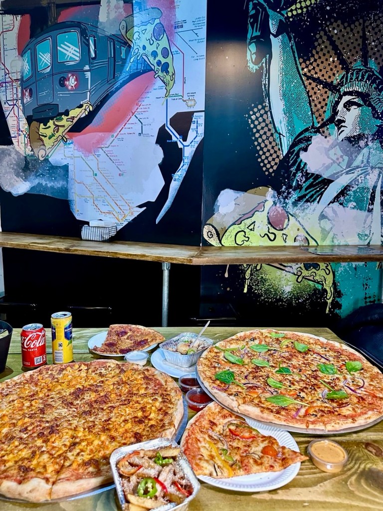 A spread of Firestone Artisan Pizza’s menu, featuring large 20” pizzas, New York-style slices, and sides on a table.