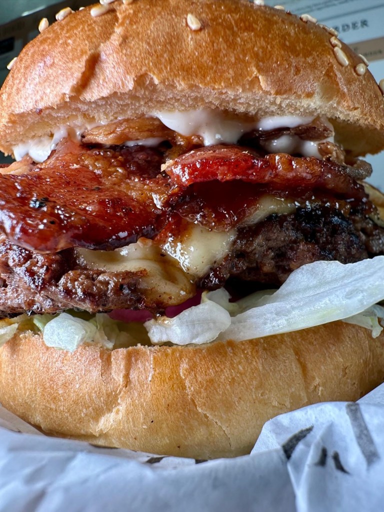 A massive Spicy Chipotle Burger loaded with jalapeños, crispy bacon, and smoky chipotle mayo, stacked high on a fresh brioche bun.