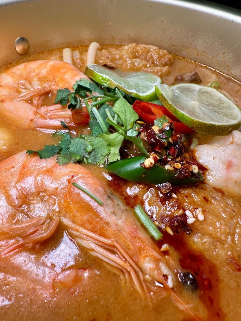 A close-up of fresh, juicy prawns in a steaming Malatang bowl, served with a flavorful tom yum broth and vegetables.