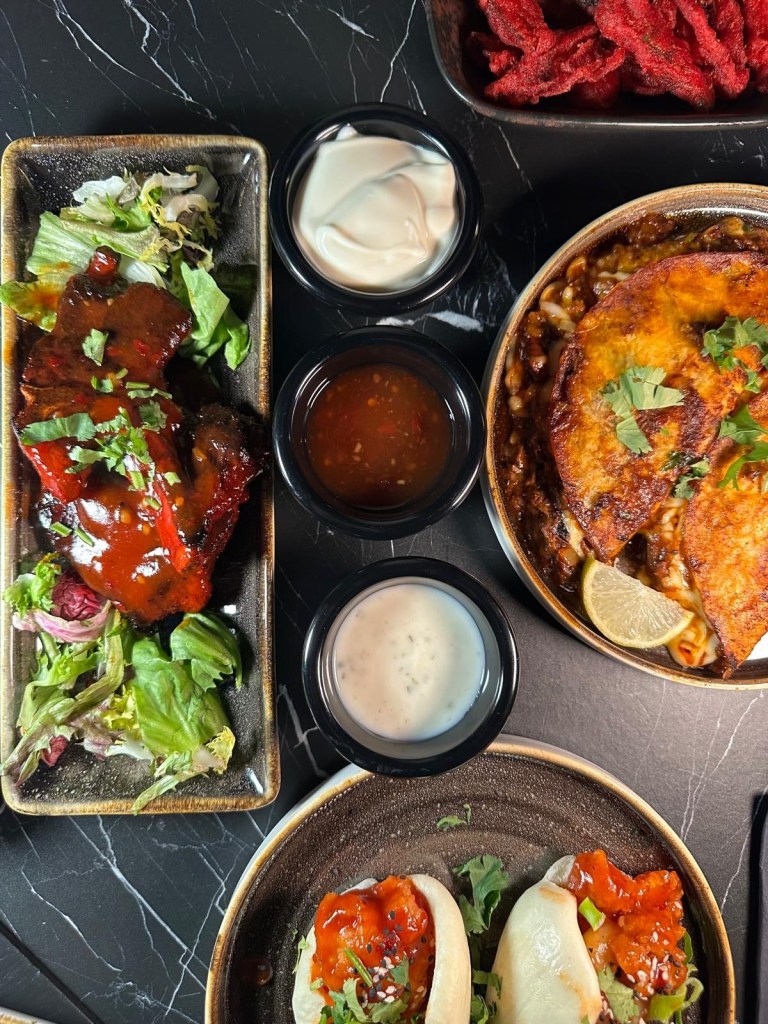 A spread of small plates from The Chamber South Shields, featuring bao buns, birria tacos, sushi rolls, lamb chops, kebabs, and crispy okra fries.