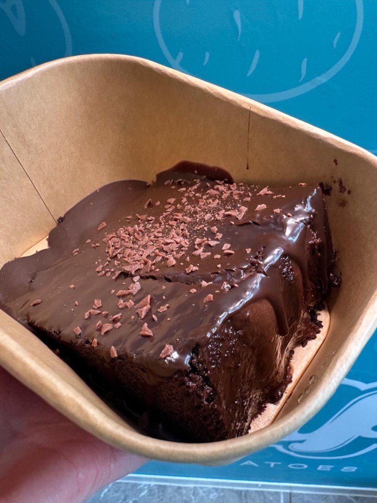 A rich and moist slice of Matilda chocolate cake from Spud Life Newcastle, dusted with cocoa and served on a white plate.