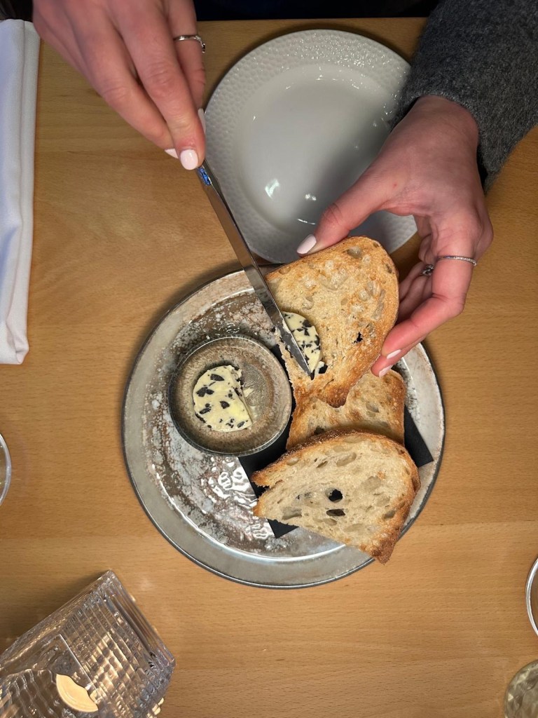 A plate of freshly baked bread with a golden crust, served with a side of smooth, creamy olive butter.