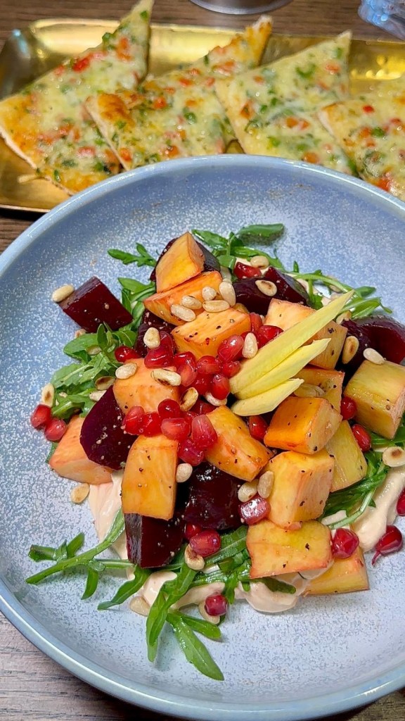 A vibrant salad with fresh mango slices, beetroot, crisp salad leaves, pomegranate seeds, and a creamy yogurt base.