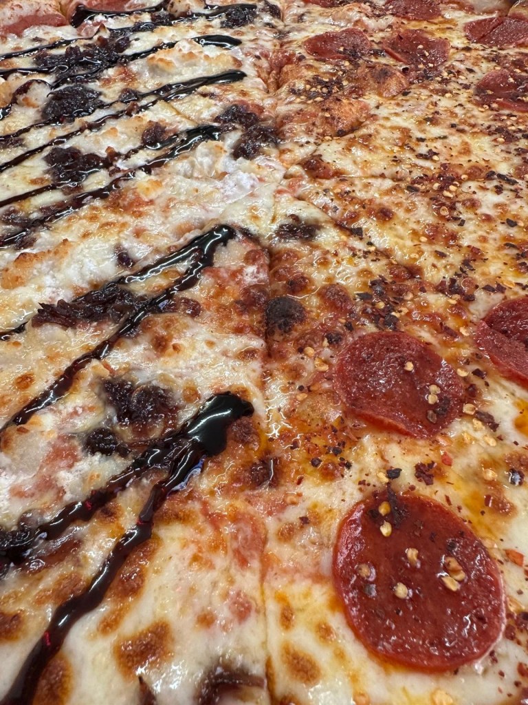 A large 20-inch New York-style pizza, half topped with spicy pepperoni and honey drizzle, and half with creamy goat’s cheese and red onion jam, served on a thin, crispy crust.