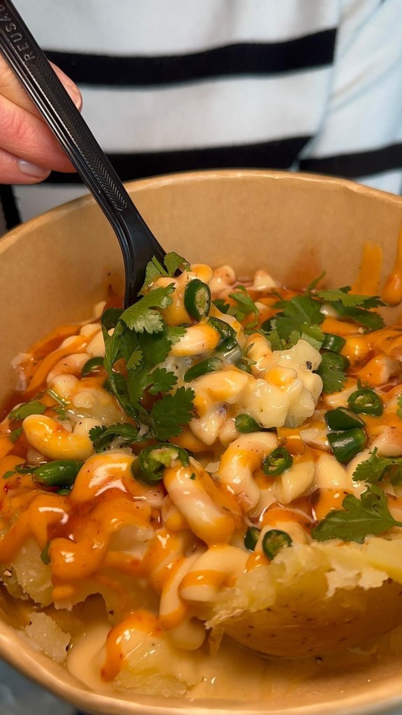 The Mac Daddy baked potato from Spud Life Newcastle, topped with creamy mac and cheese, crispy onions, Cajun spice, grated cheese, and chipotle sauce.