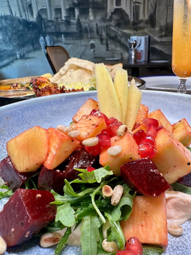 A vibrant salad with fresh mango slices, beetroot, crisp salad leaves, pomegranate seeds, and a creamy yogurt base.
