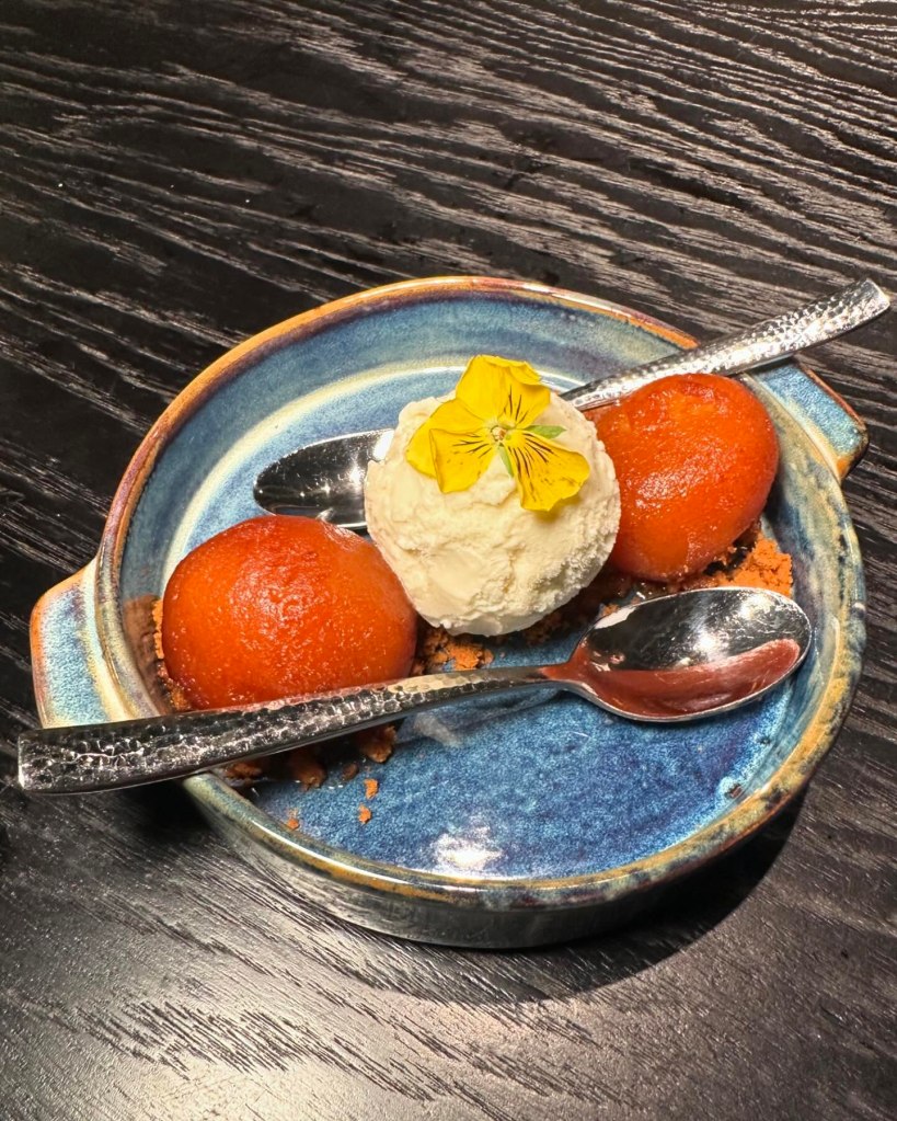 A bowl of golden Gulab Jamun, soaked in sweet syrup and garnished with crushed nuts.