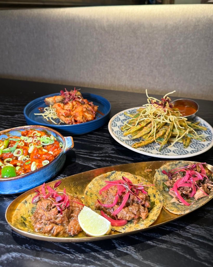 A serving of Desi tacos with vibrant toppings, including fresh herbs, pickled onions, and a drizzle of tangy sauce.