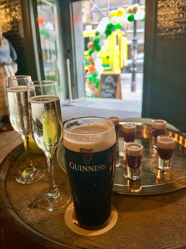 A selection of drinks at Katie O’Brien’s, including a Baby Guinness paddle board, a pint of Guinness, cocktails, and prosecco, served on a wooden bar counter.
