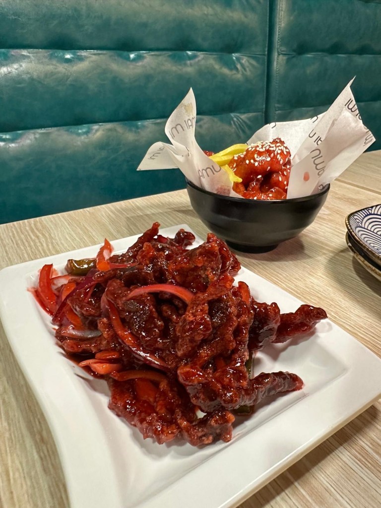 A plate of crispy beef coated in a sticky, glossy sauce, garnished with sesame seeds and spring onions.