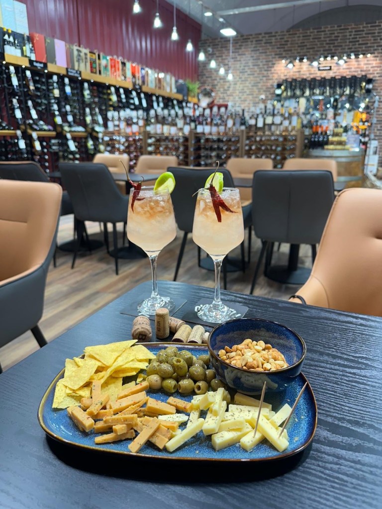 A beautifully presented cocktail with a red chilli garnish, paired with a snack platter of olives, cheese, and nuts at Newcastle Cavavin.