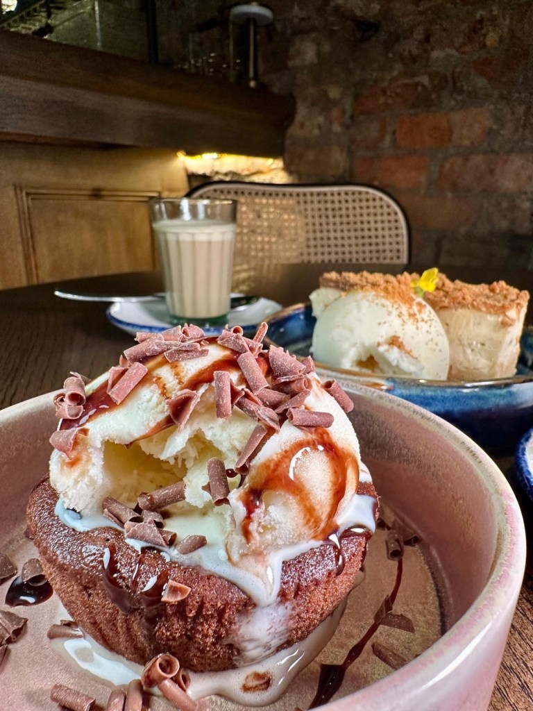 A decadent chocolate bomb dessert, served with warm sauce being poured over to reveal a rich, gooey center.