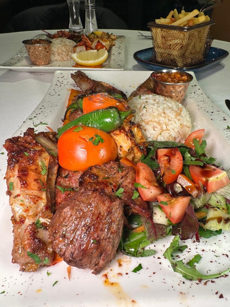 A sizzling hot mixed grill platter with marinated lamb, chicken shish, adana, ribs, and a lamb cutlet, served with rice and salad at Turknaz Restaurant.