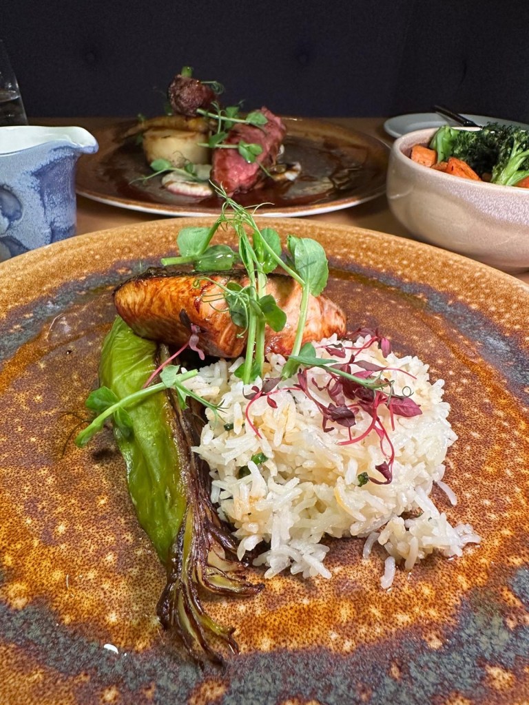 A plate of glazed salmon with miso-roasted Hispi cabbage, crispy onions, and a drizzle of chili oil.