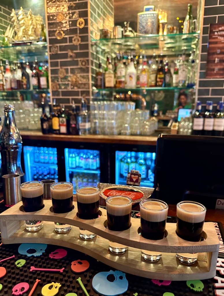 A wooden paddle board holding six Baby Guinness shots, layered with rich coffee liqueur and smooth Irish cream.