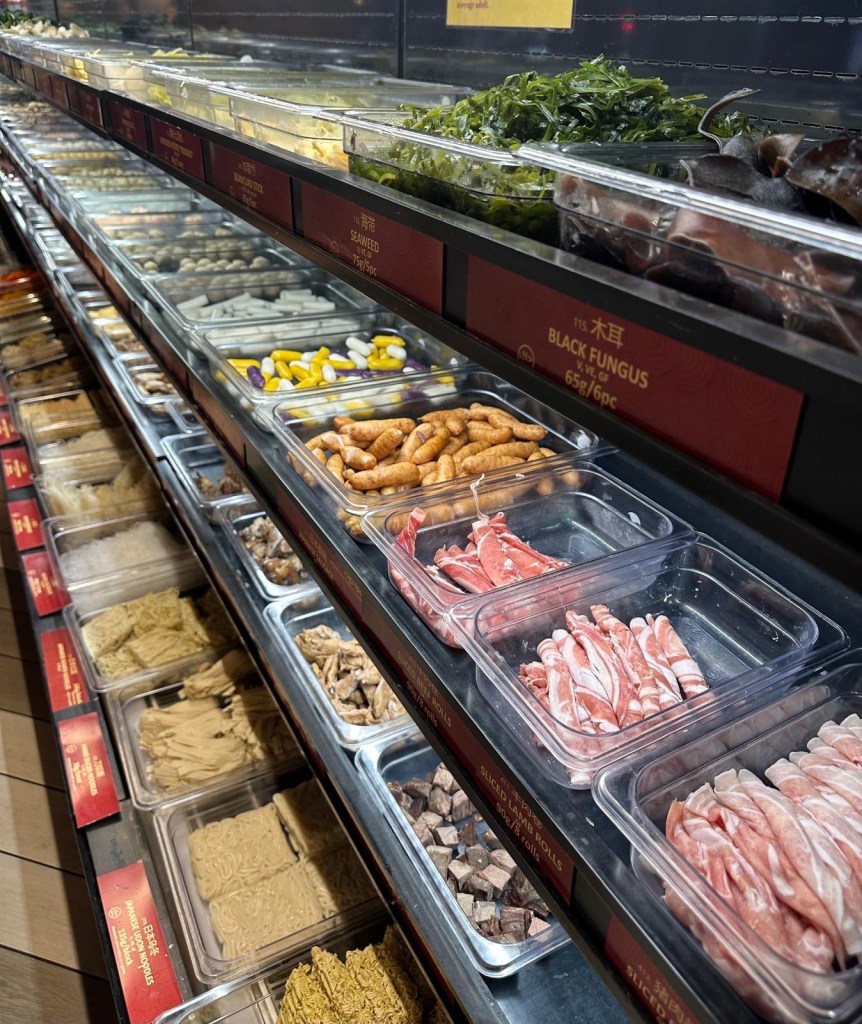A well-stocked selection fridge at Malatang Express, filled with fresh vegetables, meats, seafood, and noodles for a custom Malatang bowl.