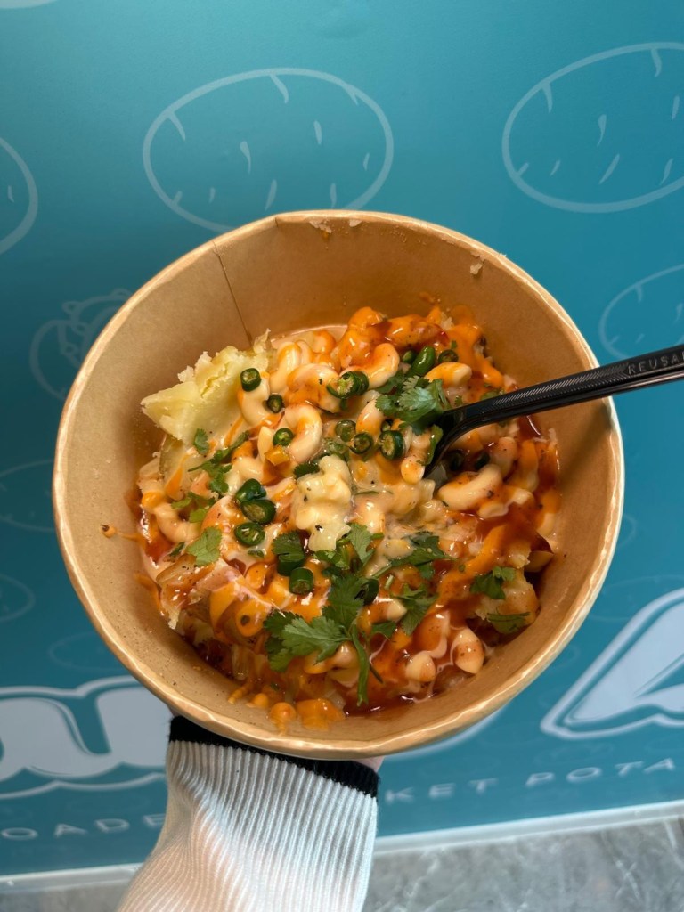 The Mac Daddy baked potato from Spud Life Newcastle, topped with creamy mac and cheese, crispy onions, Cajun spice, grated cheese, and chipotle sauce.