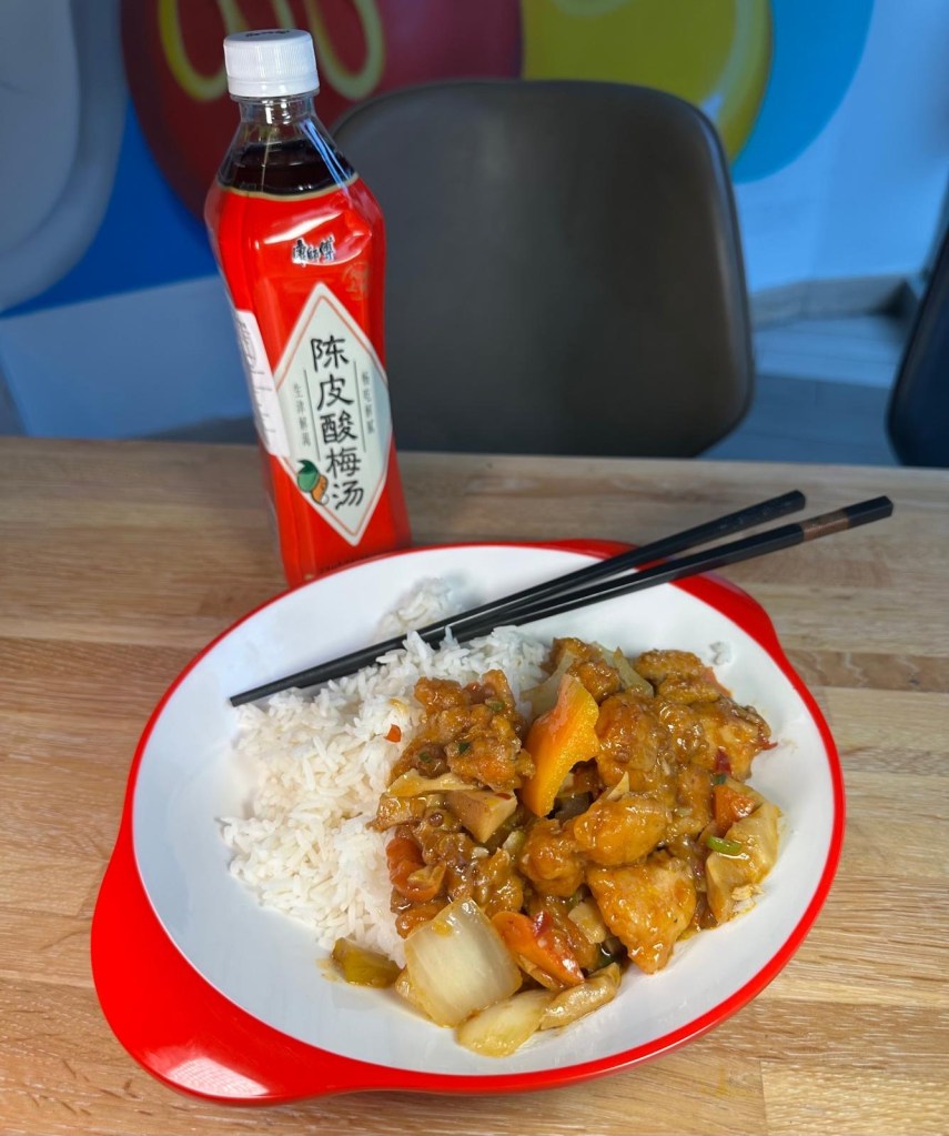 A neatly presented bento box with Kung Poo chicken, fluffy white rice, and a side of fresh vegetables.